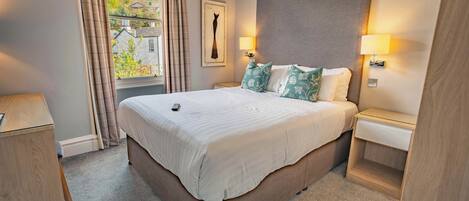 Une chambre d’hôtel avec un grand lit, deux tables de chevet, une fenêtre avec des rideaux et une lampe fixée au mur.