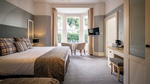 A hotel room with a large bed, a desk with a chair, a television, and a view of the outdoors through a window. - Ambleside Townhouse (Ambleside)