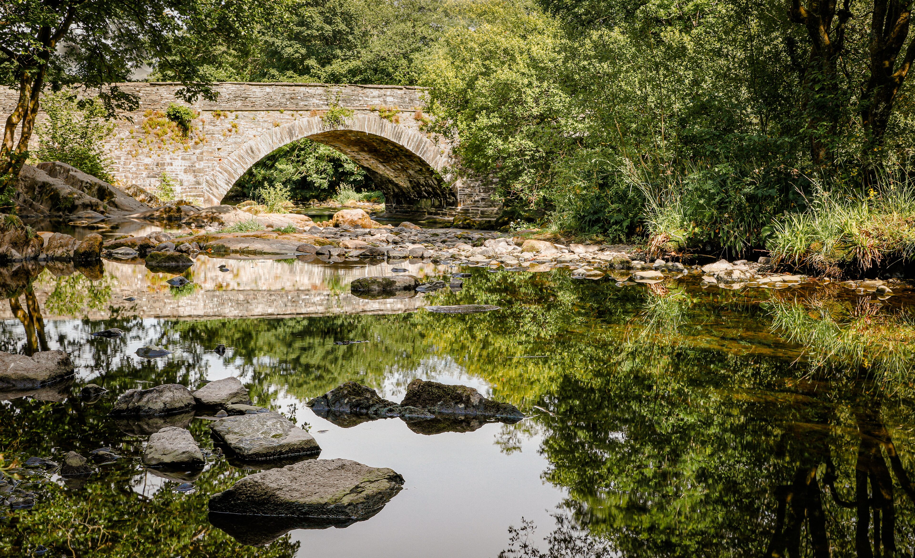 Un pont de pierre enjambe une rivière paisible, entouré d’une végétation luxuriante.