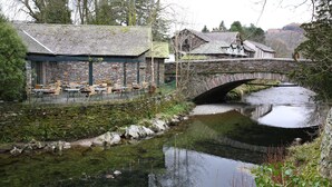 A stone bridge over a calm river, a stone building with outdoor seating, and a mountainous backdrop. - Ambleside Townhouse (Ambleside)
