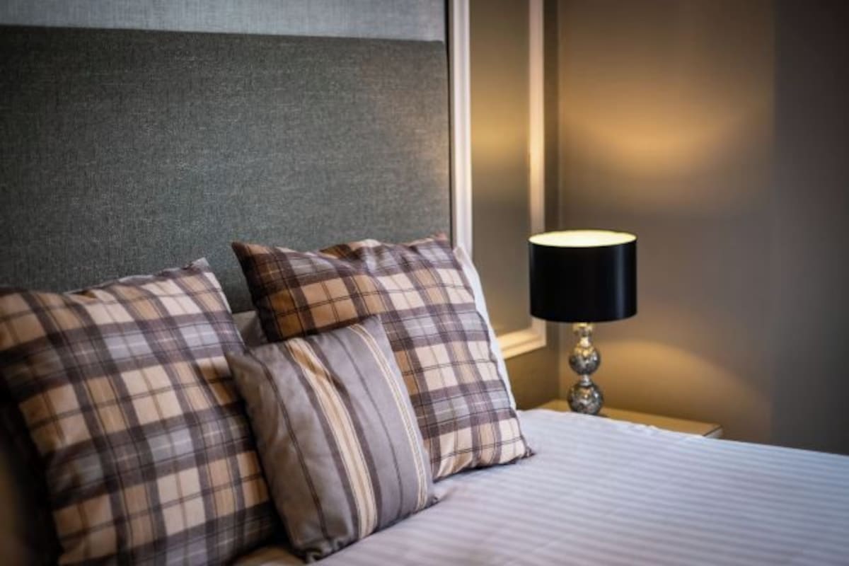 Una cama bien hecha con ropa de cama escocesa y una lámpara de noche.