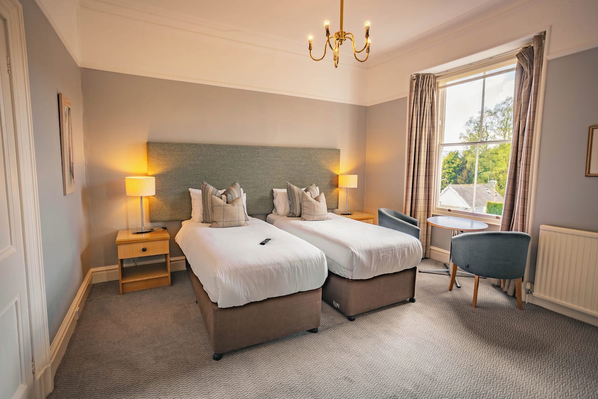 A hotel room with two single beds, a desk, a chair, and a window with curtains.