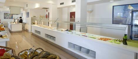 Un espace buffet avec différents stands de nourriture, une personne qui sert, et des paniers de pain.