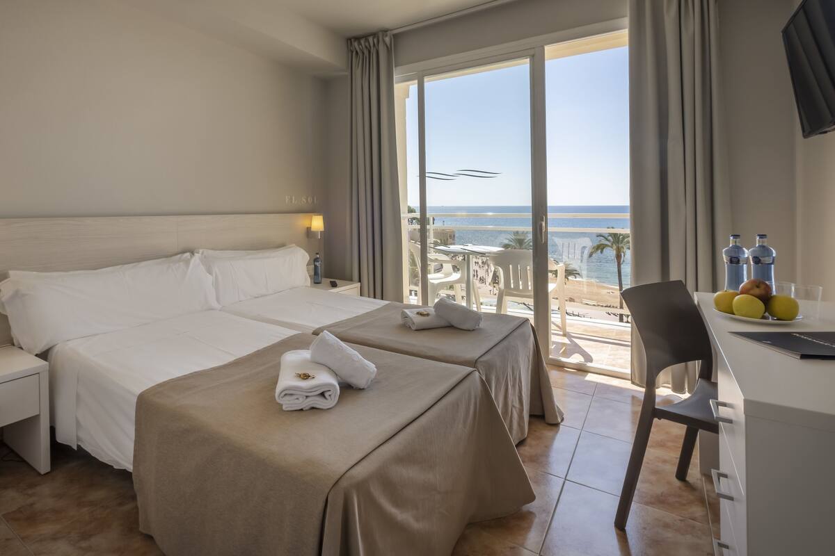 A hotel room with two beds, a desk with a chair, a phone, and a view of the beach.
