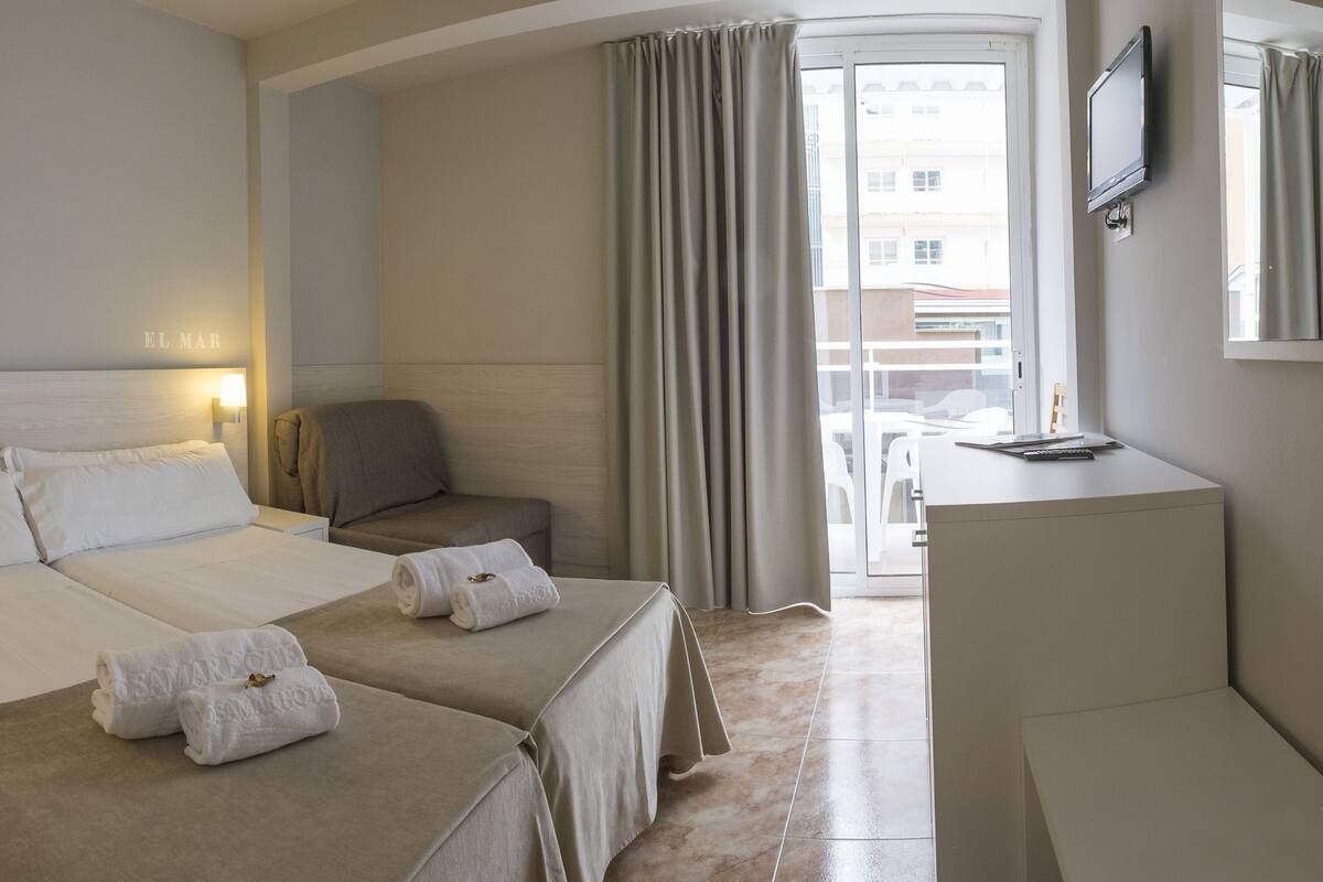 A hotel room with two beds, a desk, a chair, and a TV.