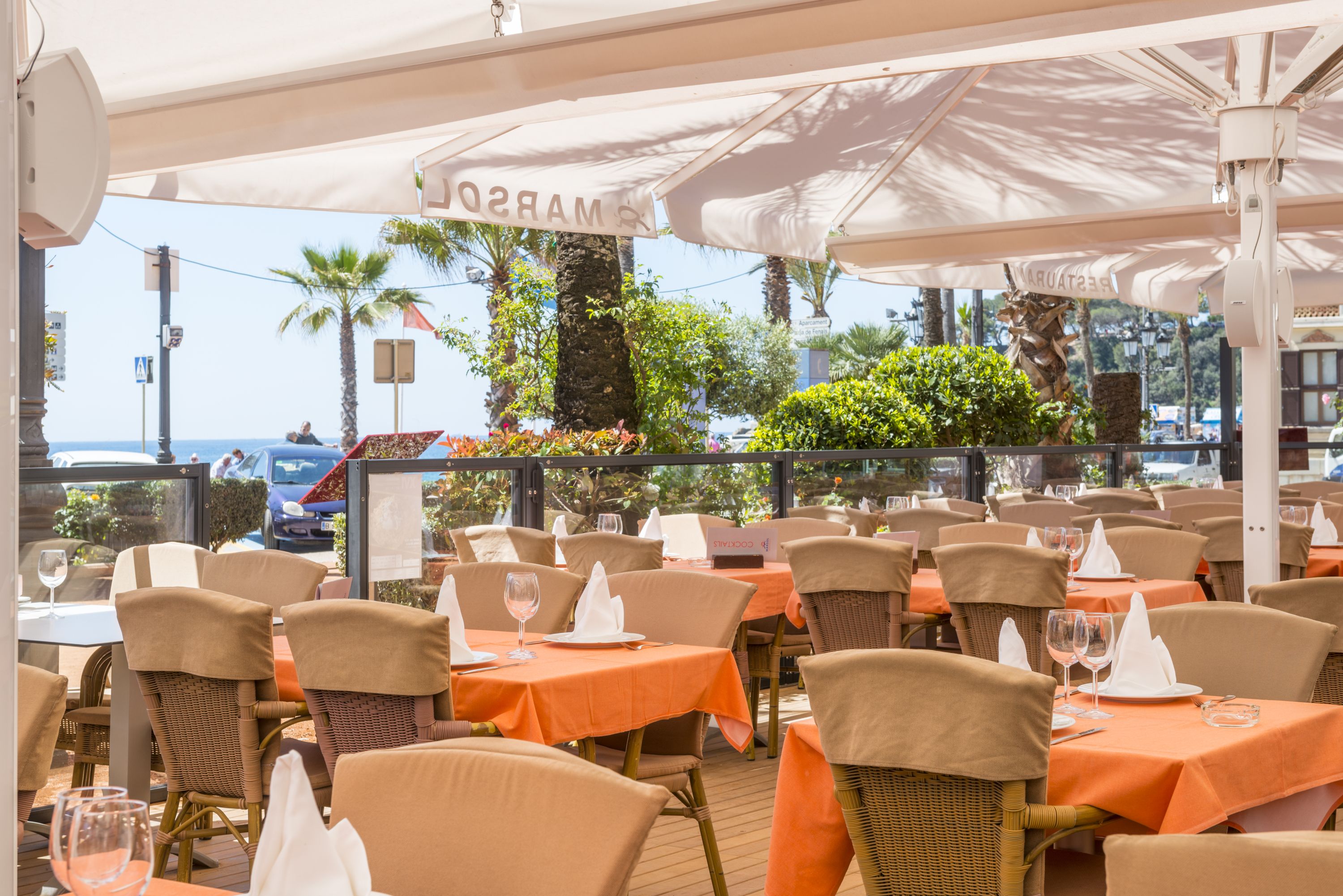 Un espace extérieur aménagé pour les repas, avec des tables, des chaises, des parasols et une vue sur la mer.
