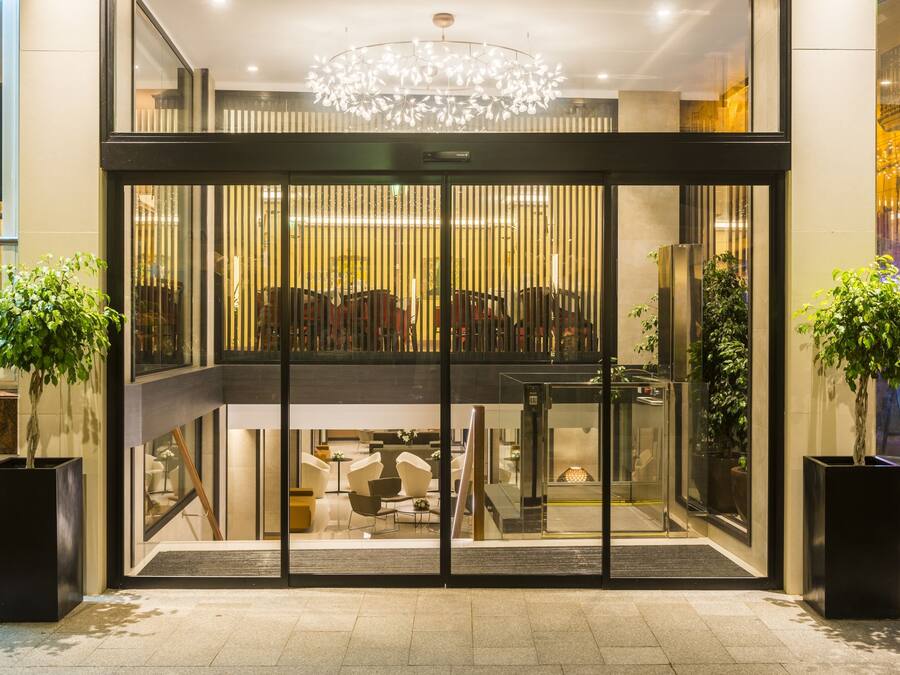 A modern hotel entrance with a glass door, a chandelier, and potted plants.