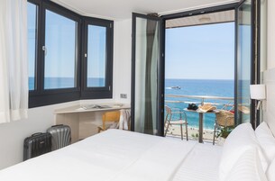 A hotel room with a bed, a desk, a chair, and a view of the sea.