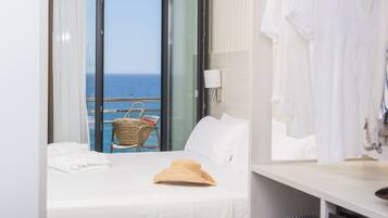 A hotel room with a bed, a suitcase, a straw hat, and a view of the sea through a large window.