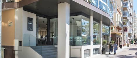 Um hotel moderno com fachada de vidro, área de estar externa e entrada visível com degraus.