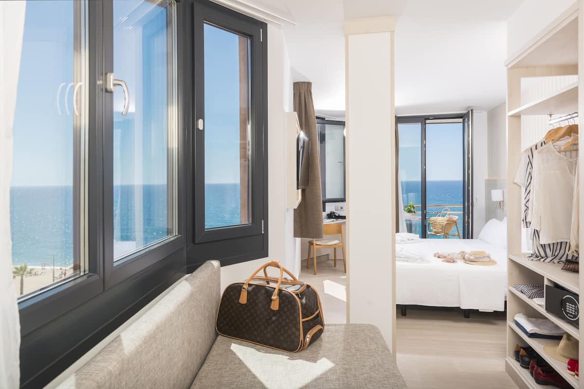 A hotel room with a large window, a bed, a desk, and a wardrobe.