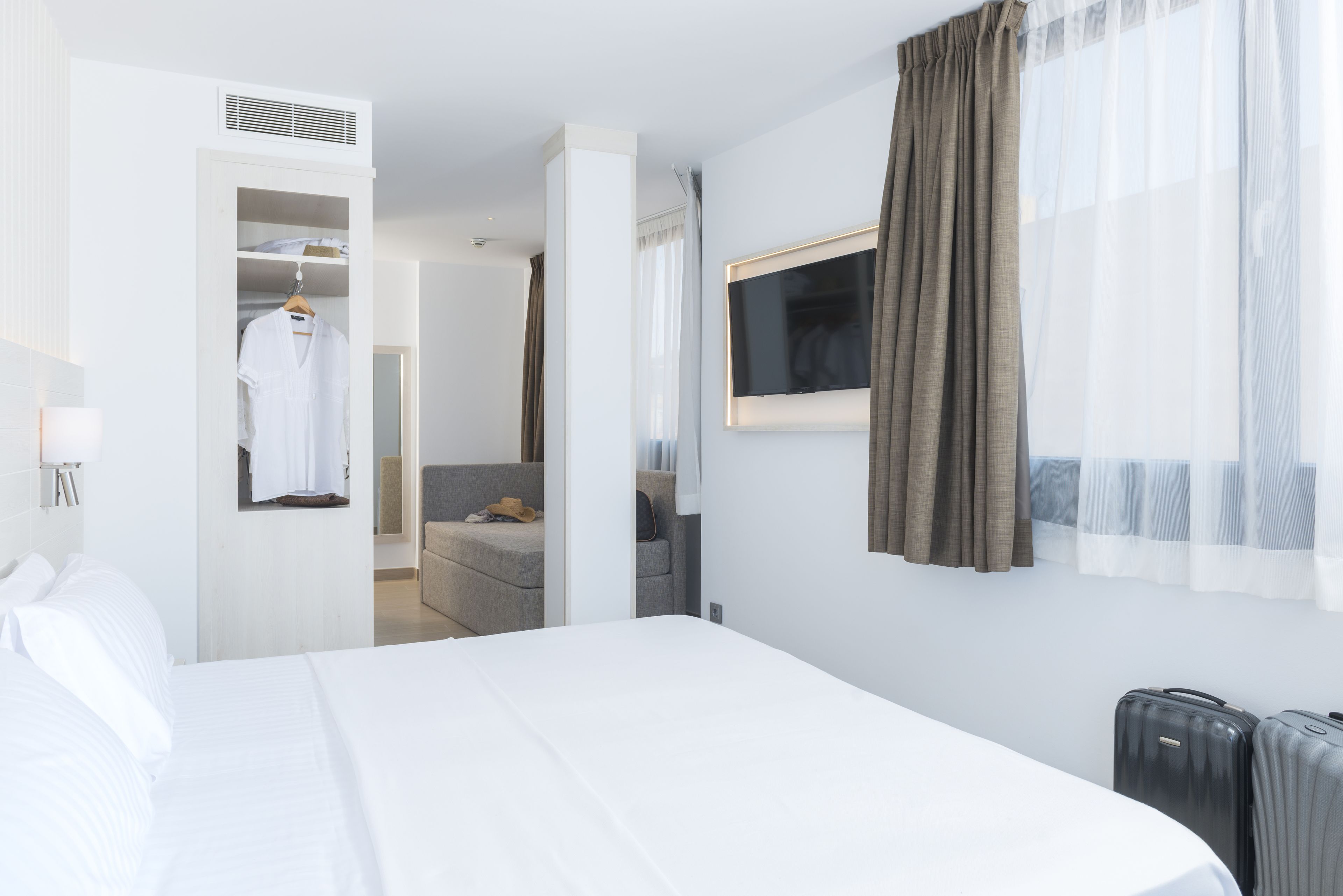 Ein Hotelzimmer mit Bett, Wandfernseher, Schrank und einer Sitzecke mit Sofa und Tisch.