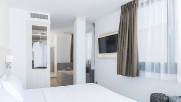 A hotel room with a bed, a TV mounted on the wall, a wardrobe, and a seating area with a sofa and a table.
