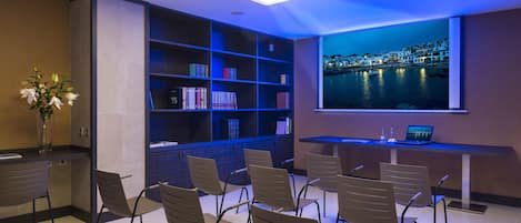 A conference room with a projector, a bookshelf, a laptop, and a view of a coastal town.