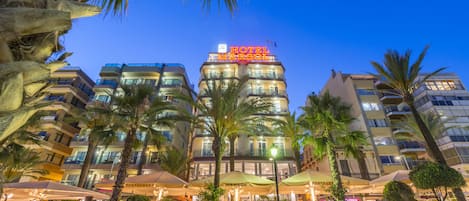 A hotel with a prominent sign, outdoor seating, and palm trees.