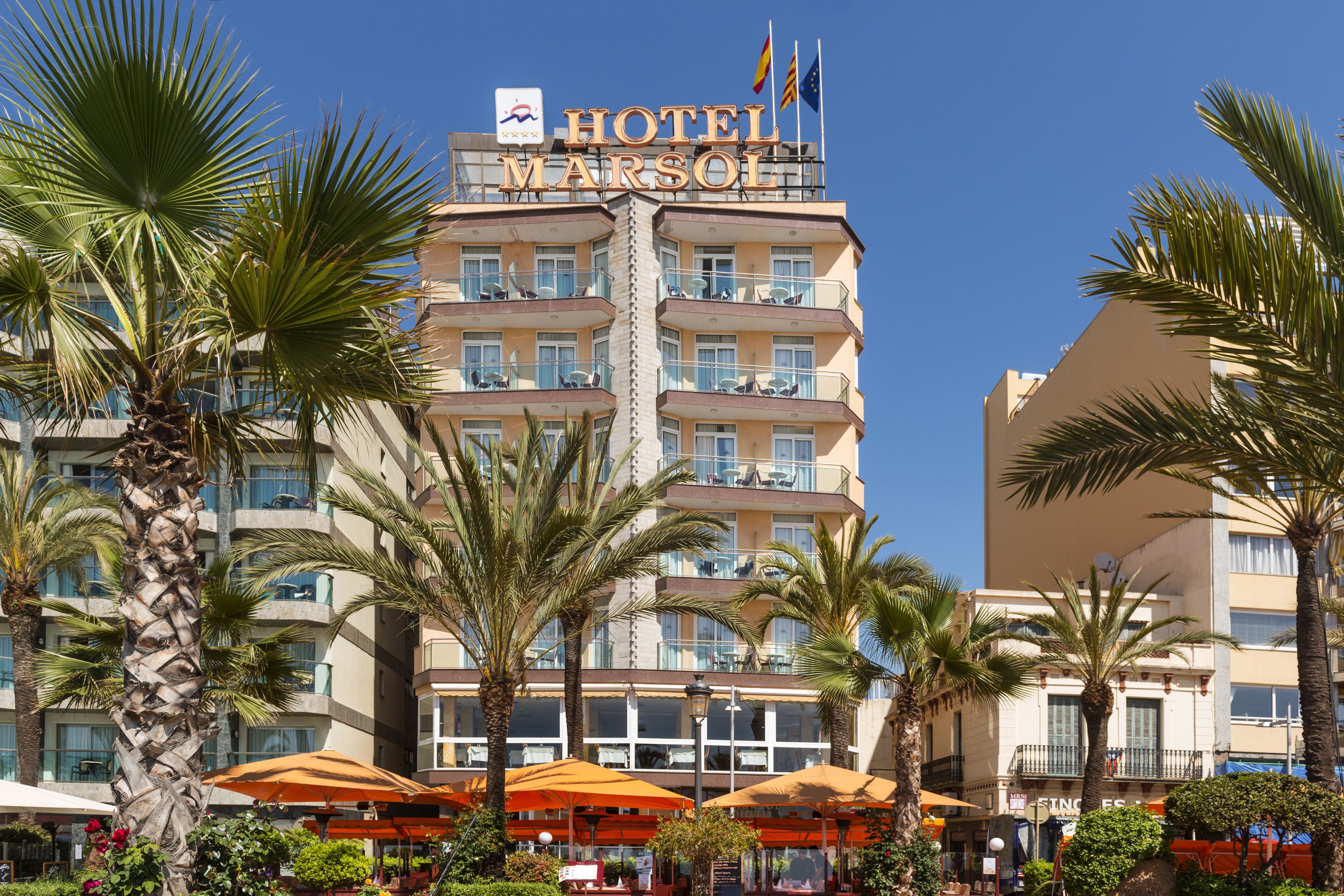 Un hotel de varios pisos con balcones, palmeras y zonas de estar al aire libre.