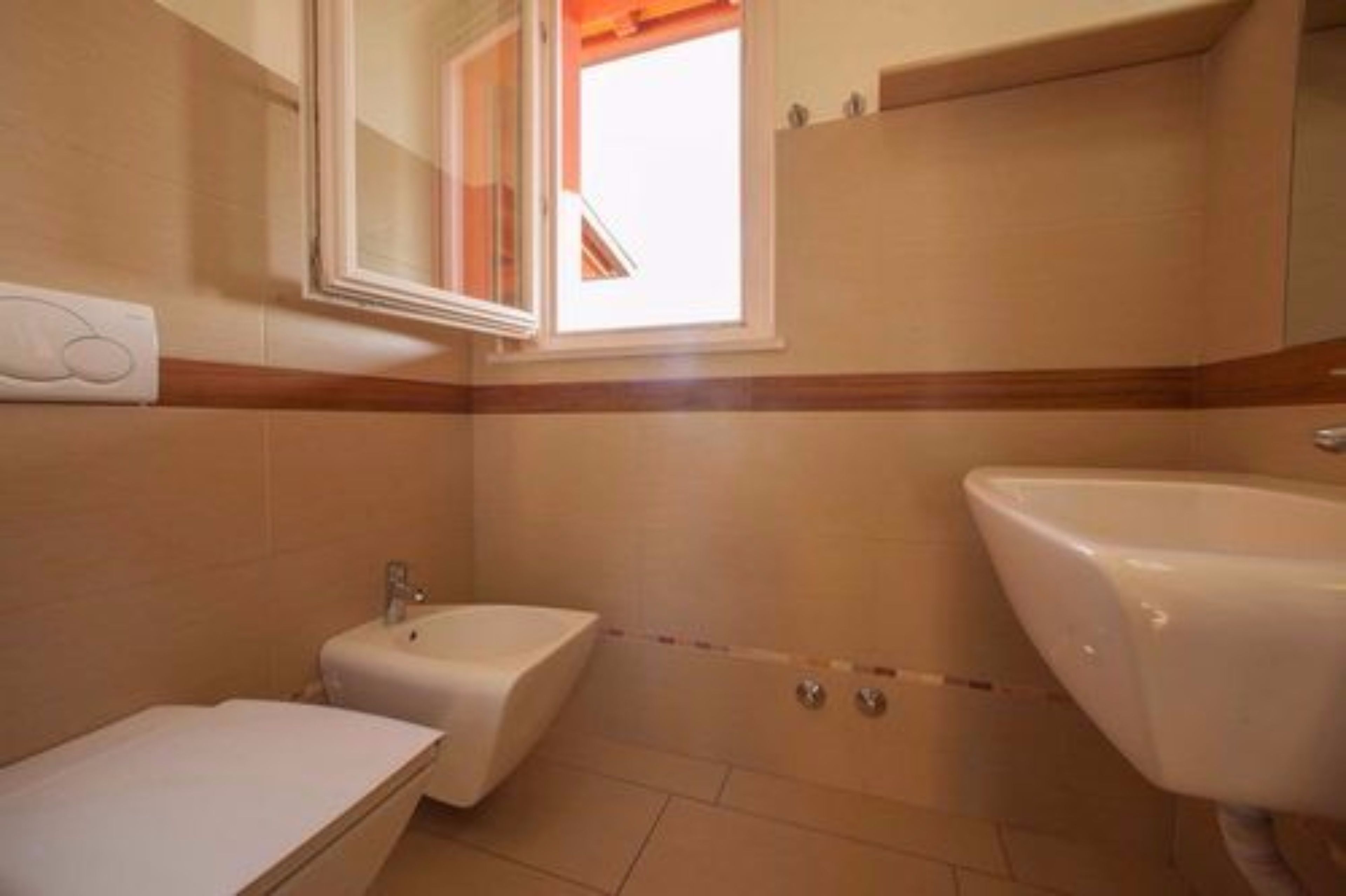 A bathroom with a sink, bidet, and a window.