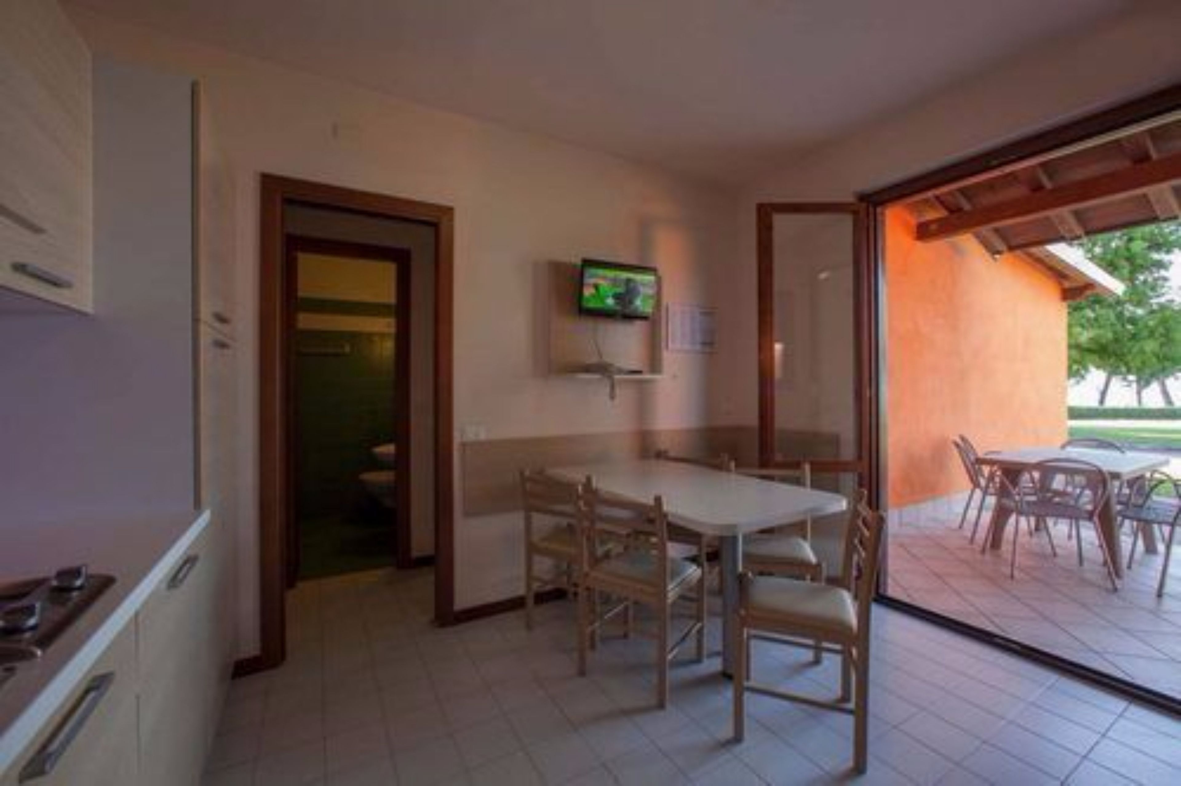 A dining area with a table and chairs, a television mounted on the wall, and a view of the outdoors through a glass door.