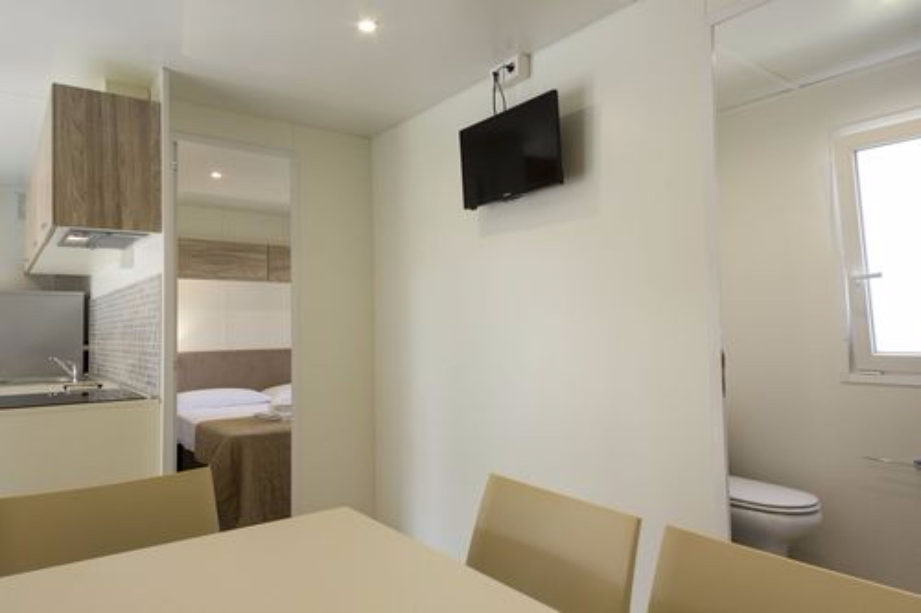 Une chambre d’hôtel compacte comprenant un coin cuisine, un lit, un téléviseur fixé au mur et une fenêtre.