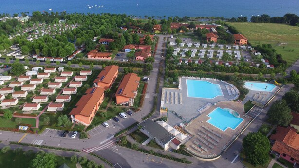Vue aérienne d’une station balnéaire comprenant de nombreux hébergements de type bungalow, une piscine centrale et, au loin, un port de plaisance.