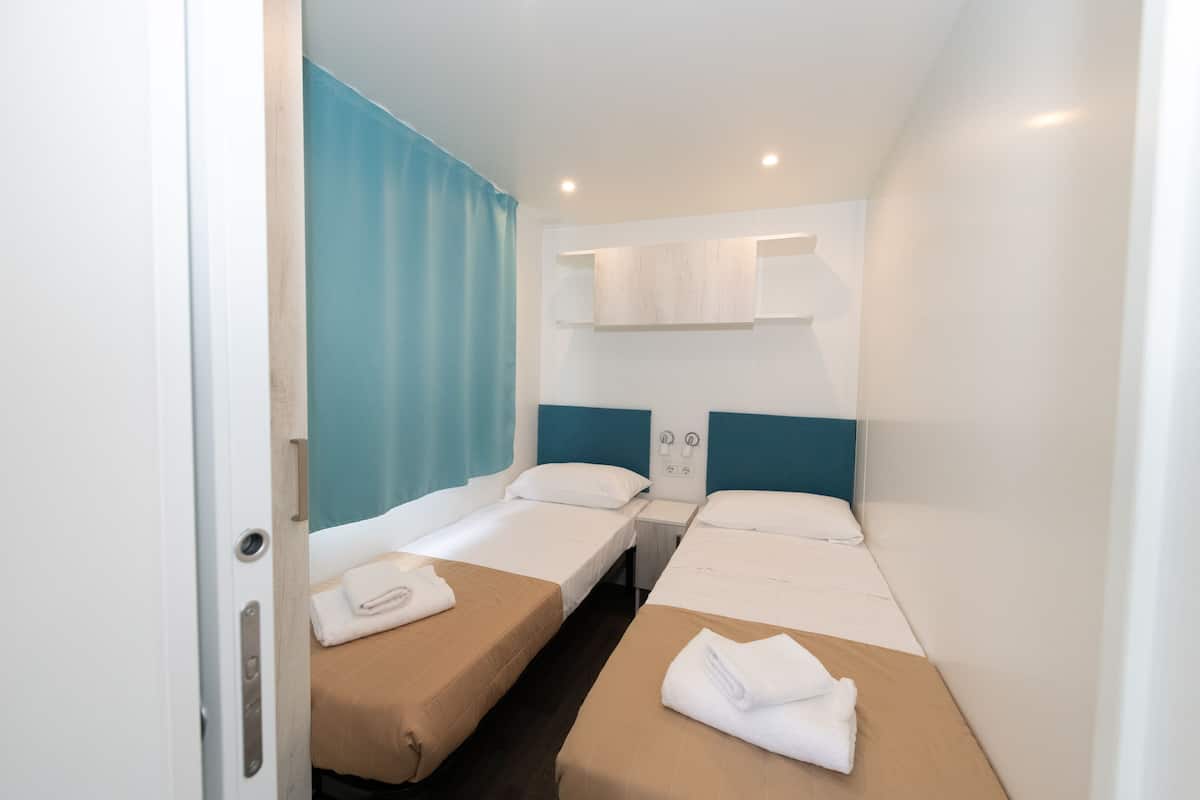 Ein kleines Hotelzimmer mit zwei Einzelbetten, einem kleinen Schreibtisch und einem Fenster mit Vorhängen.