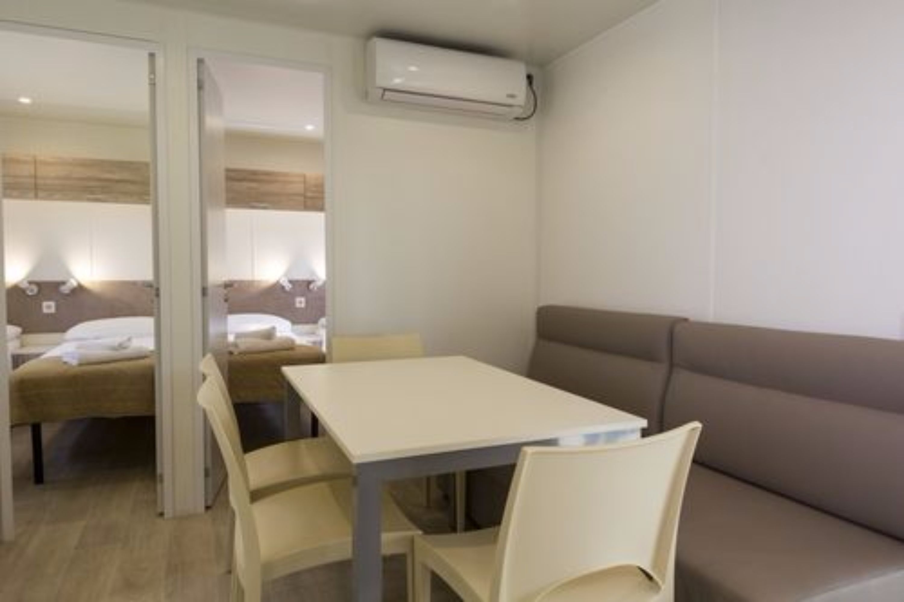 A hotel room with a bed, a table, and a sofa. There is an air conditioning unit on the wall.
