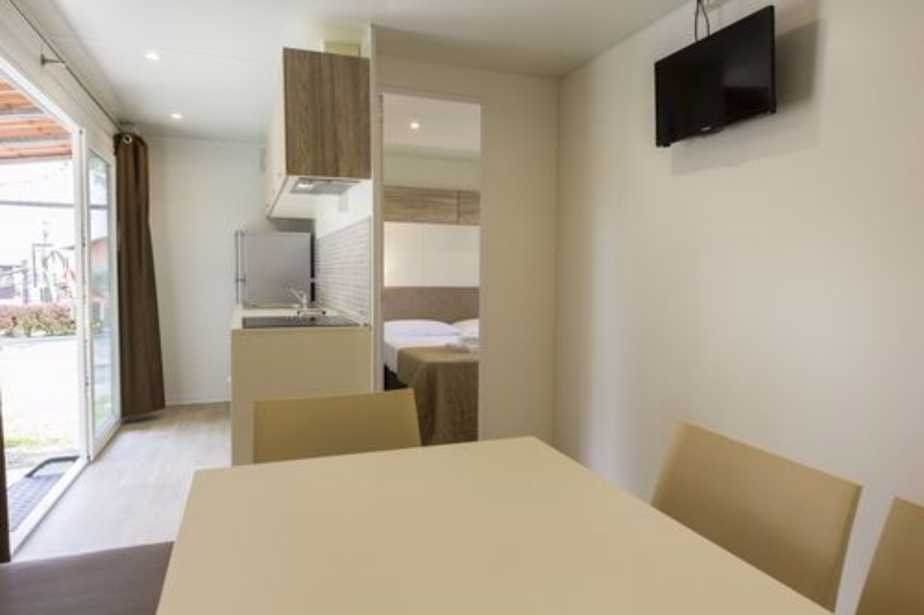 Una habitación de hotel moderna con comedor, kitchenette y televisor montado en la pared.