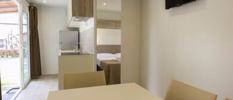 Una habitación de hotel moderna con comedor, kitchenette y televisor montado en la pared.