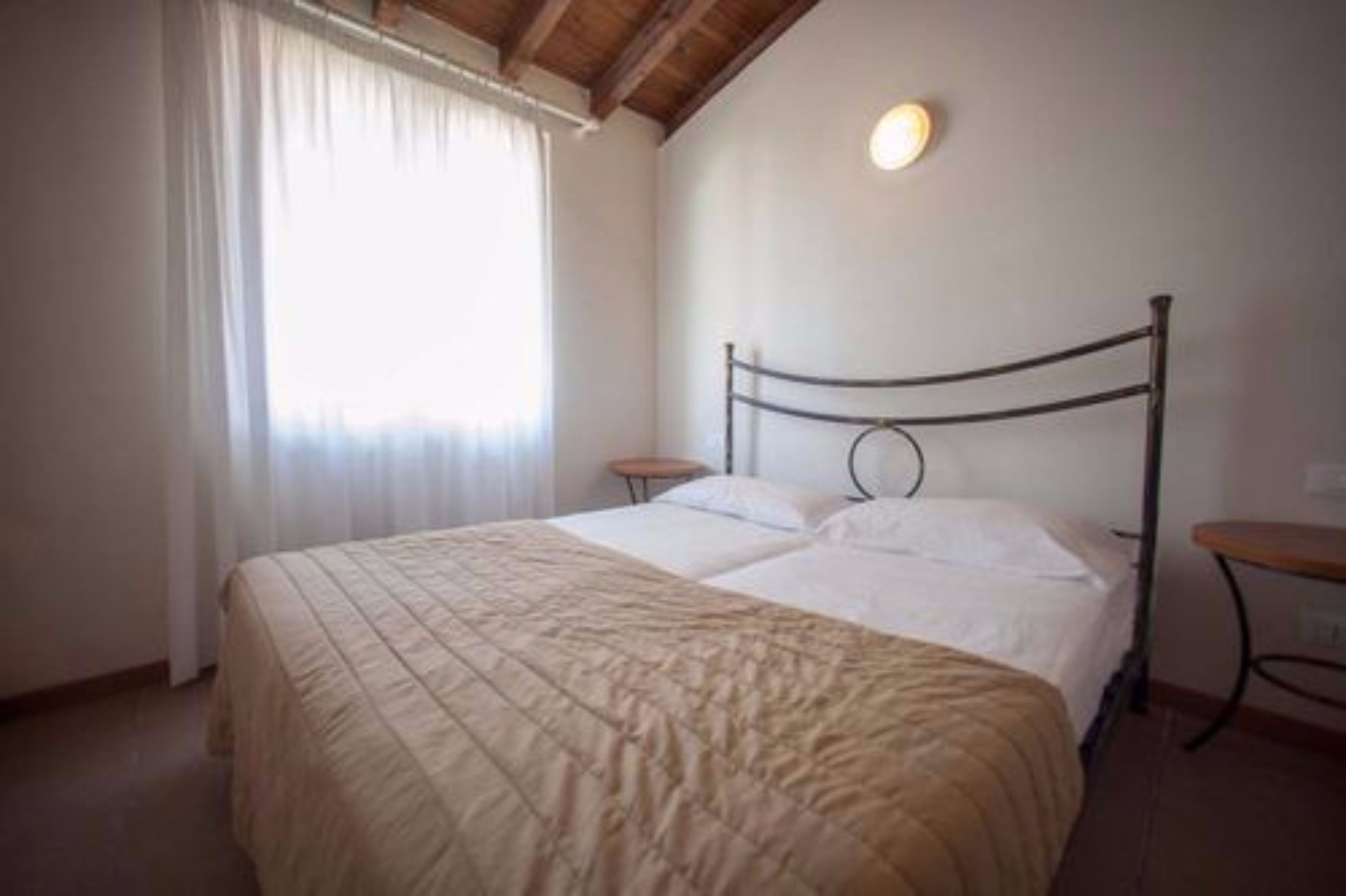 A single bed with a headboard, a bedside table, and a window with curtains.
