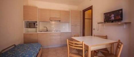 Una cocina compacta con muebles de madera, un microondas y una pequeña mesa de comedor con sillas.