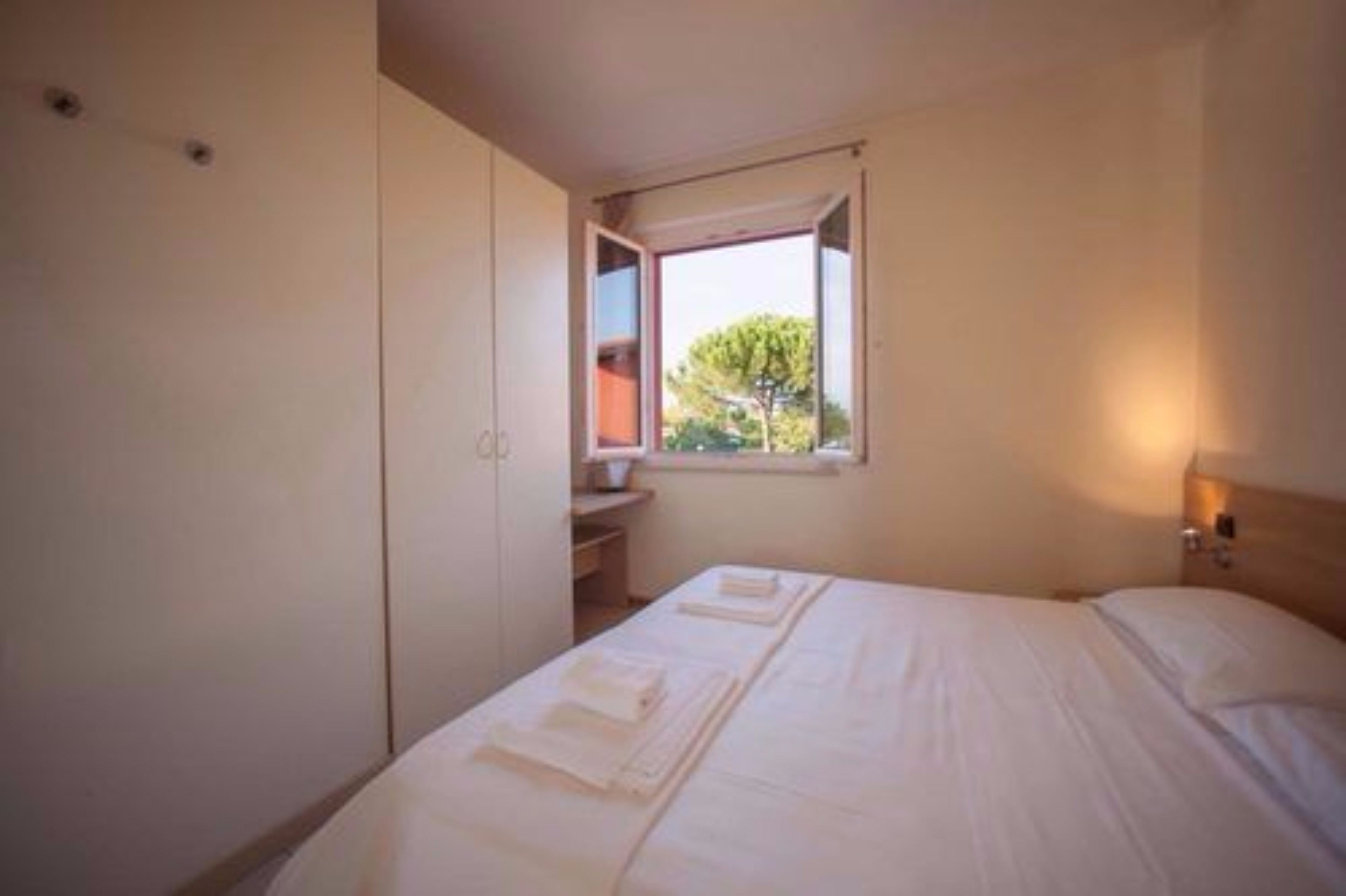 A bedroom with a bed, a wardrobe, a window, and a nightstand.