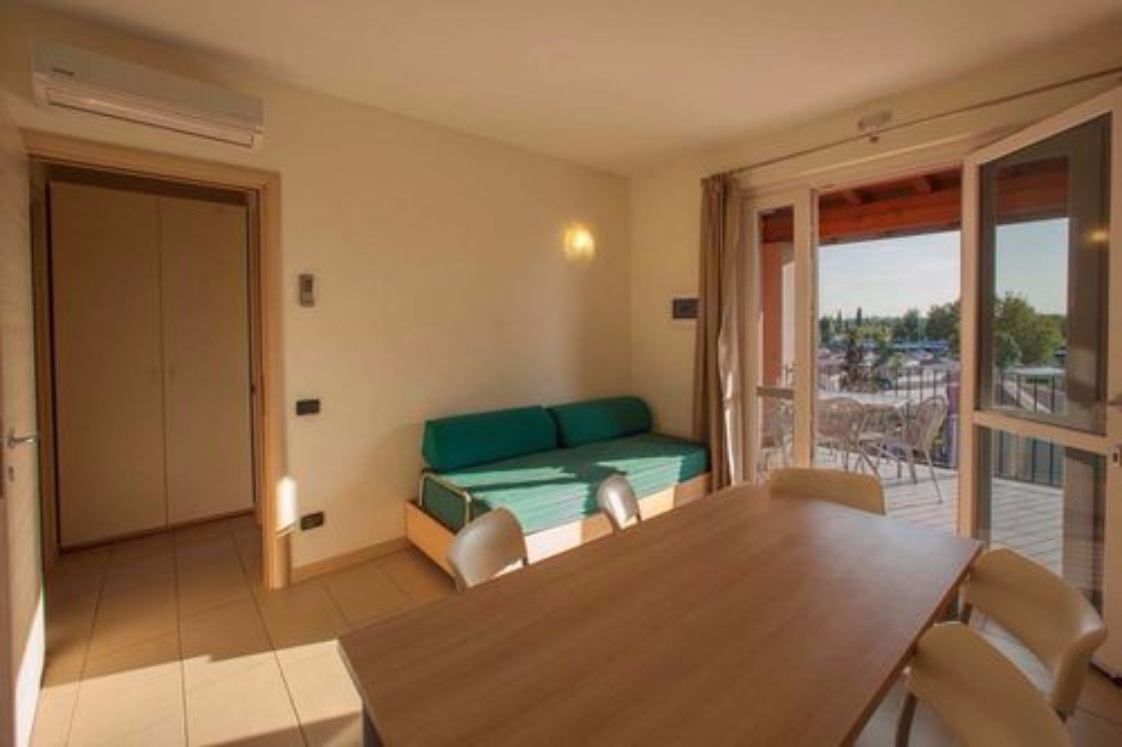 Een kamer met een houten tafel, een groene bank en een schuifdeur die leidt naar een buitenruimte.