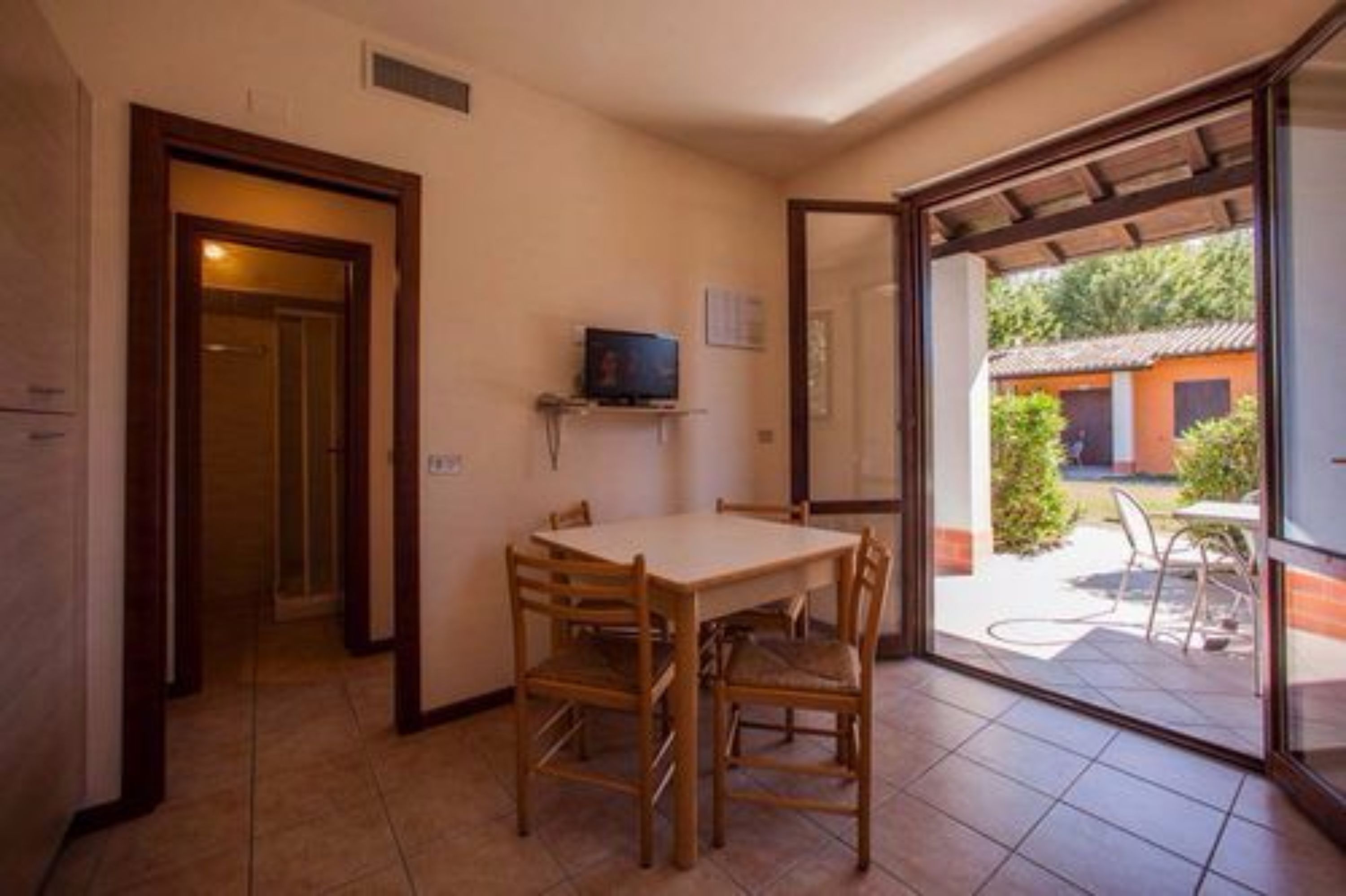 Zona pranzo con tavolo e sedie, televisore su un ripiano e vista del patio esterno.