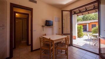 Zona pranzo con tavolo e sedie, televisore su un ripiano e vista del patio esterno.