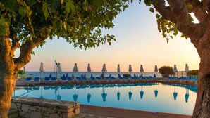 A poolside area with lounge chairs and umbrellas, overlooking a body of water. - Silva Beach Hotel (Hersonissos)