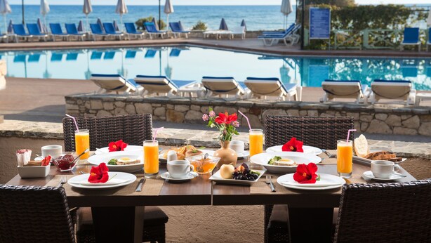 A dining table with breakfast items and a view of a pool and beach chairs. - Silva Beach Hotel (Hersonissos)
