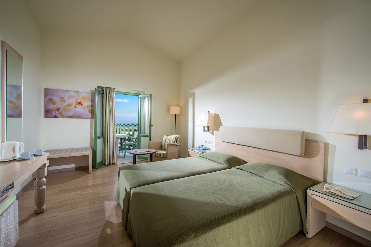 Une chambre d’hôtel avec deux lits, un bureau, une chaise, une lampe et une vue sur l’extérieur.