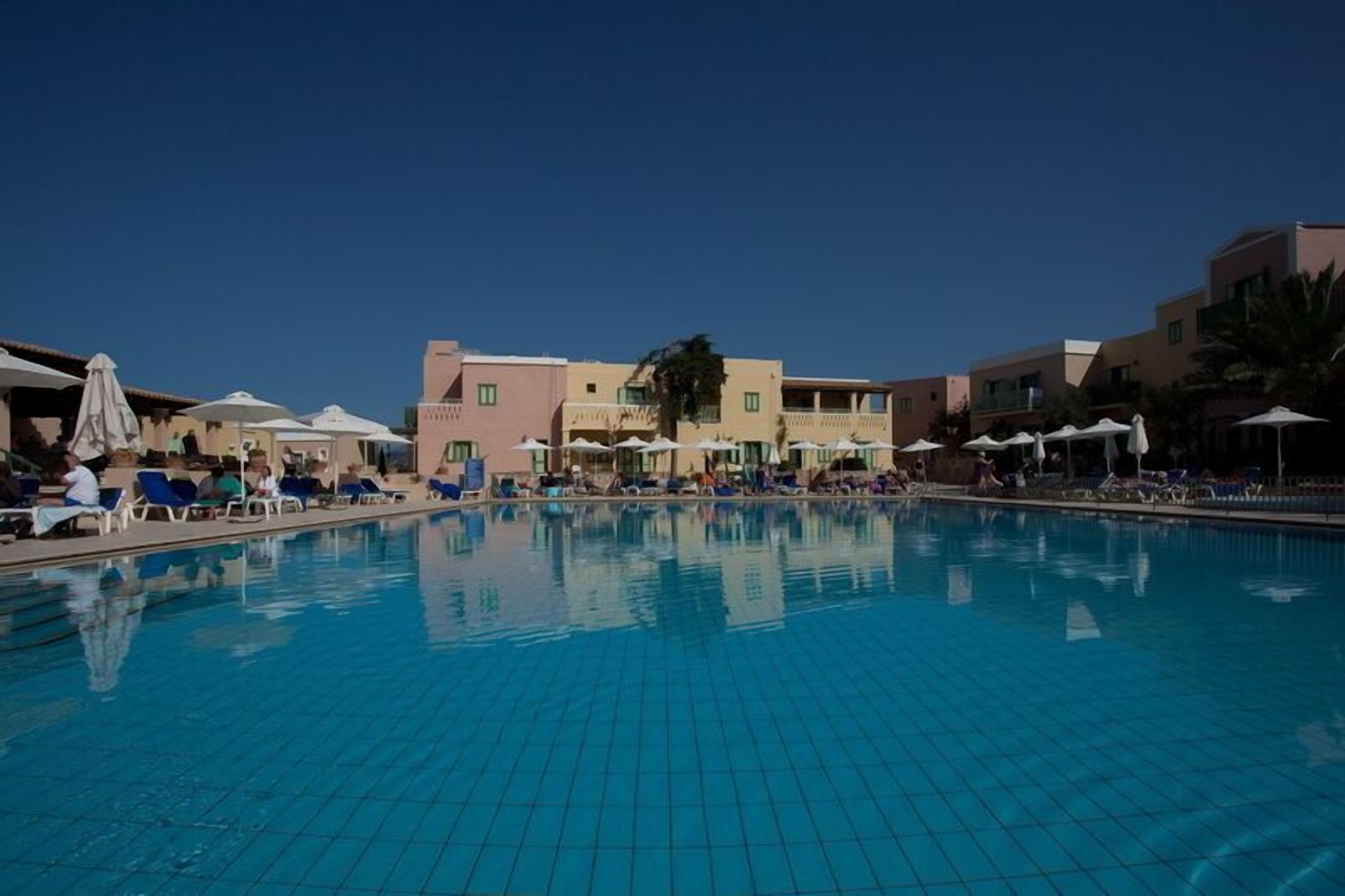A swimming pool with lounge chairs and umbrellas, surrounded by buildings with balconies.