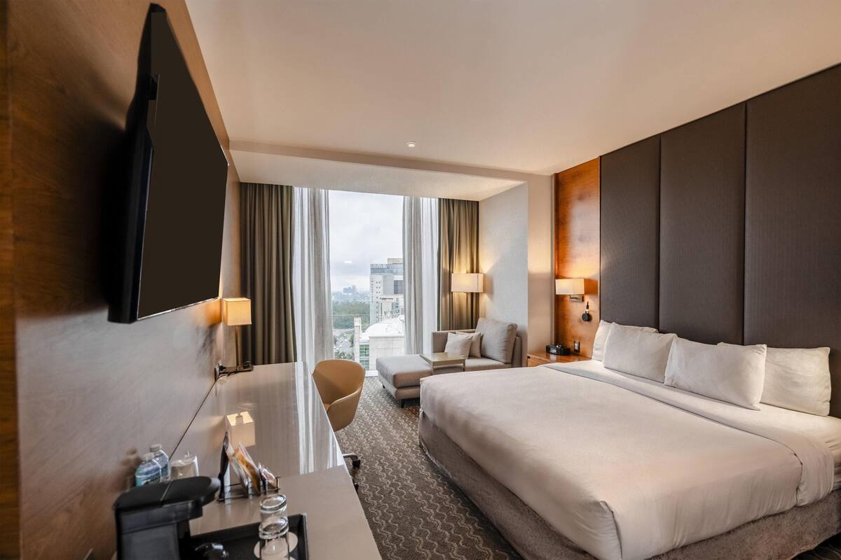 Habitación de hotel con una cama grande, un escritorio, una silla, un televisor y vistas a la ciudad.