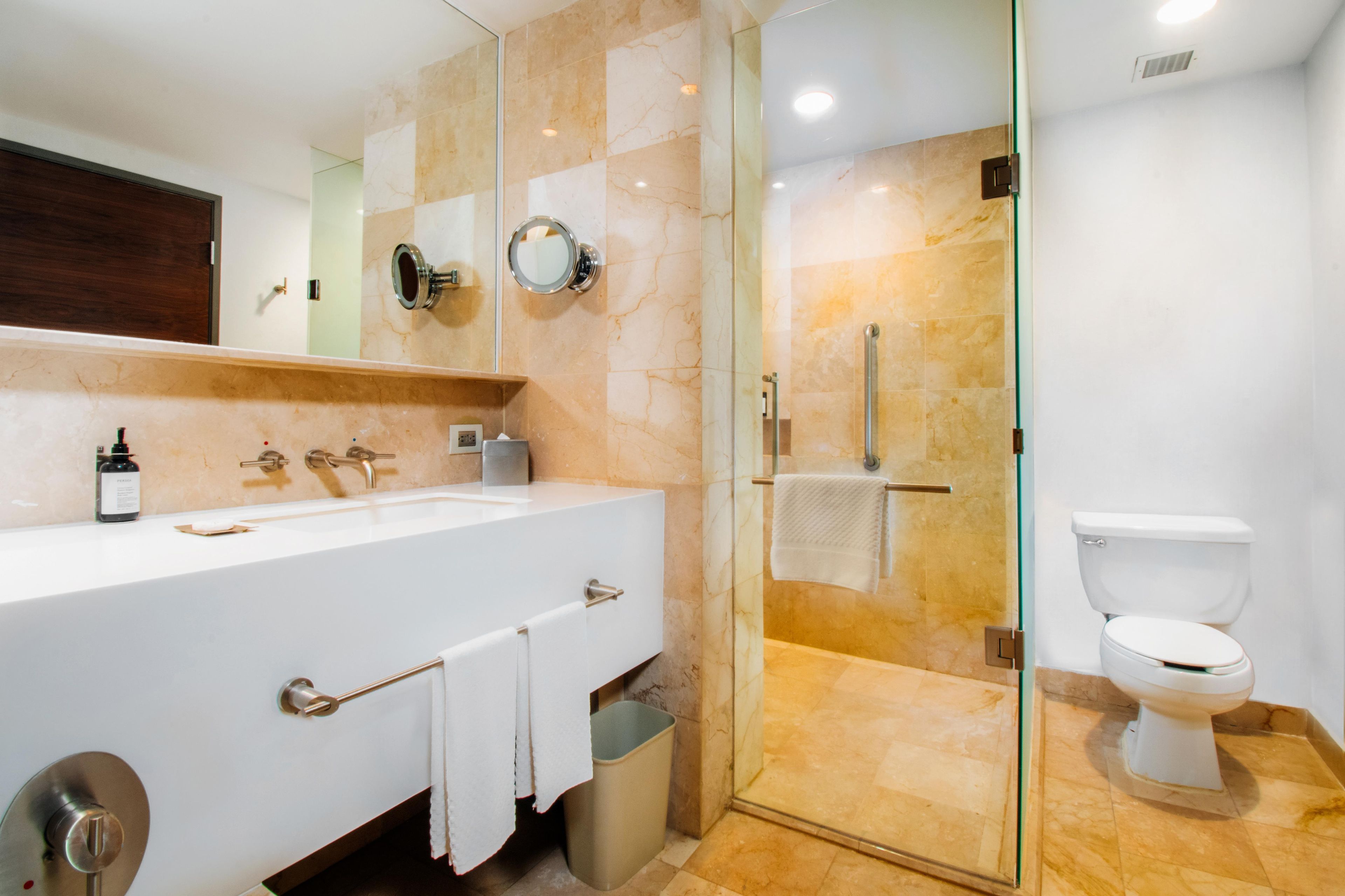 Un baño moderno con ducha envuelta en vidrio, un lavamanos blanco con espejo y un inodoro.