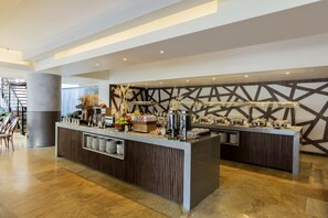 Un hall d’hôtel moderne avec un espace buffet central, un escalier et un mur décoratif.