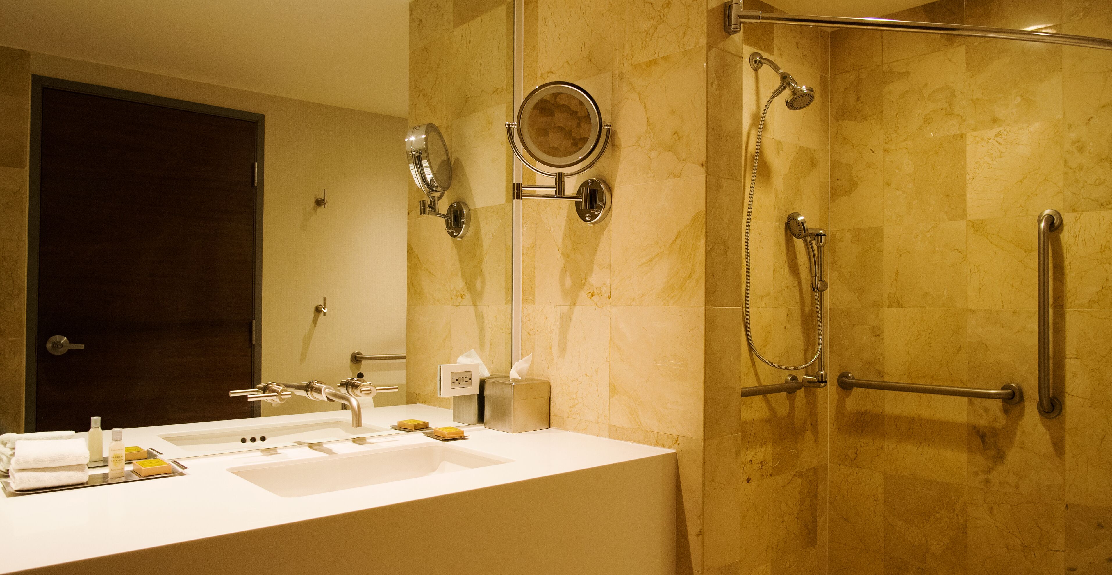 Ein Badezimmer mit Waschbecken, Spiegel, Handtuchhalter und einer Dusche mit Haltegriffen.