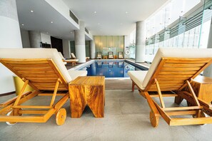 Un espace piscine avec des chaises longues en bois et une petite table en bois.