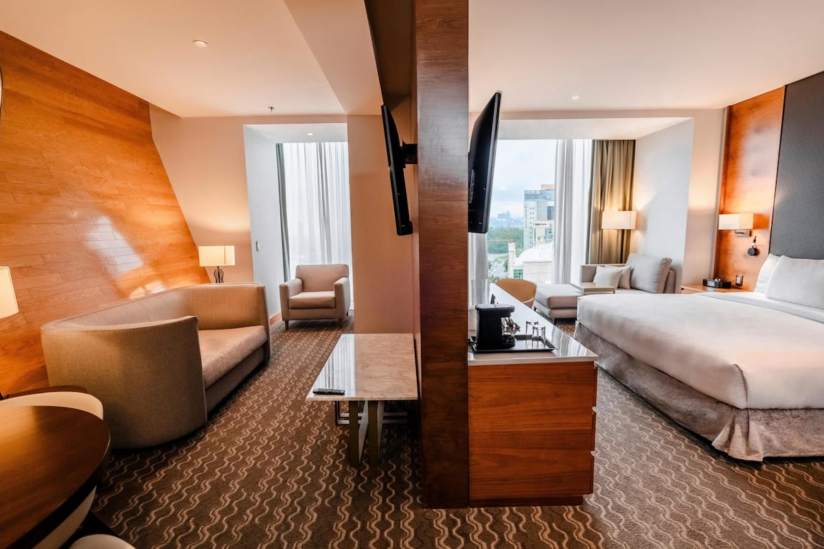 Une chambre d’hôtel équipée d’un canapé, d’un fauteuil, d’un lit, d’une télévision, d’un bureau et offrant une vue sur la ville.