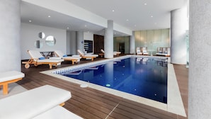 A modern indoor swimming pool with lounge chairs and a wooden deck. - DoubleTree by Hilton Hotel Mexico City Santa Fe (Mexico City)
