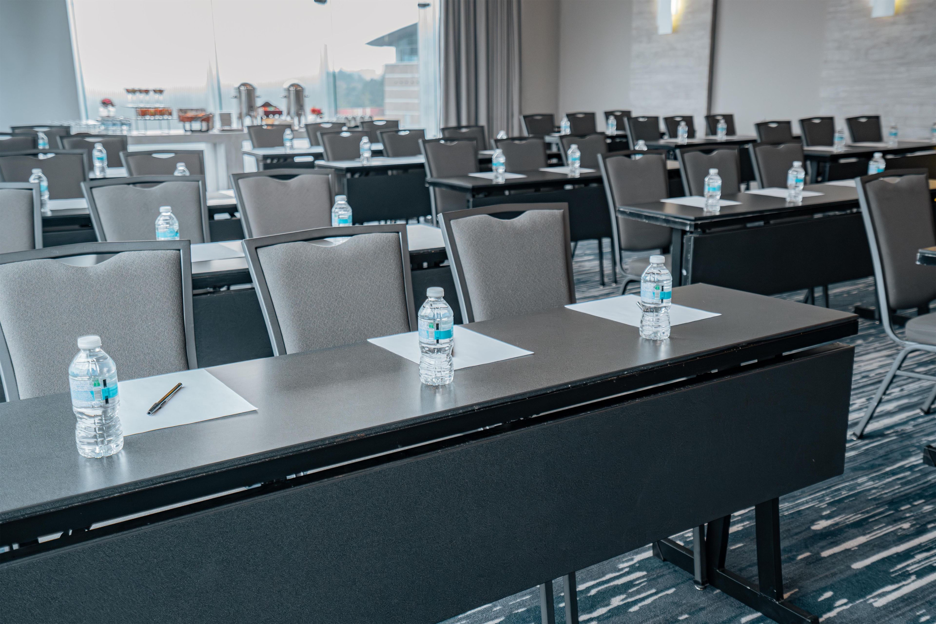 Un salón de conferencias con filas de mesas, sillas y botellas de agua.