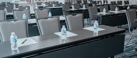 Un salón de conferencias con filas de mesas, sillas y botellas de agua.