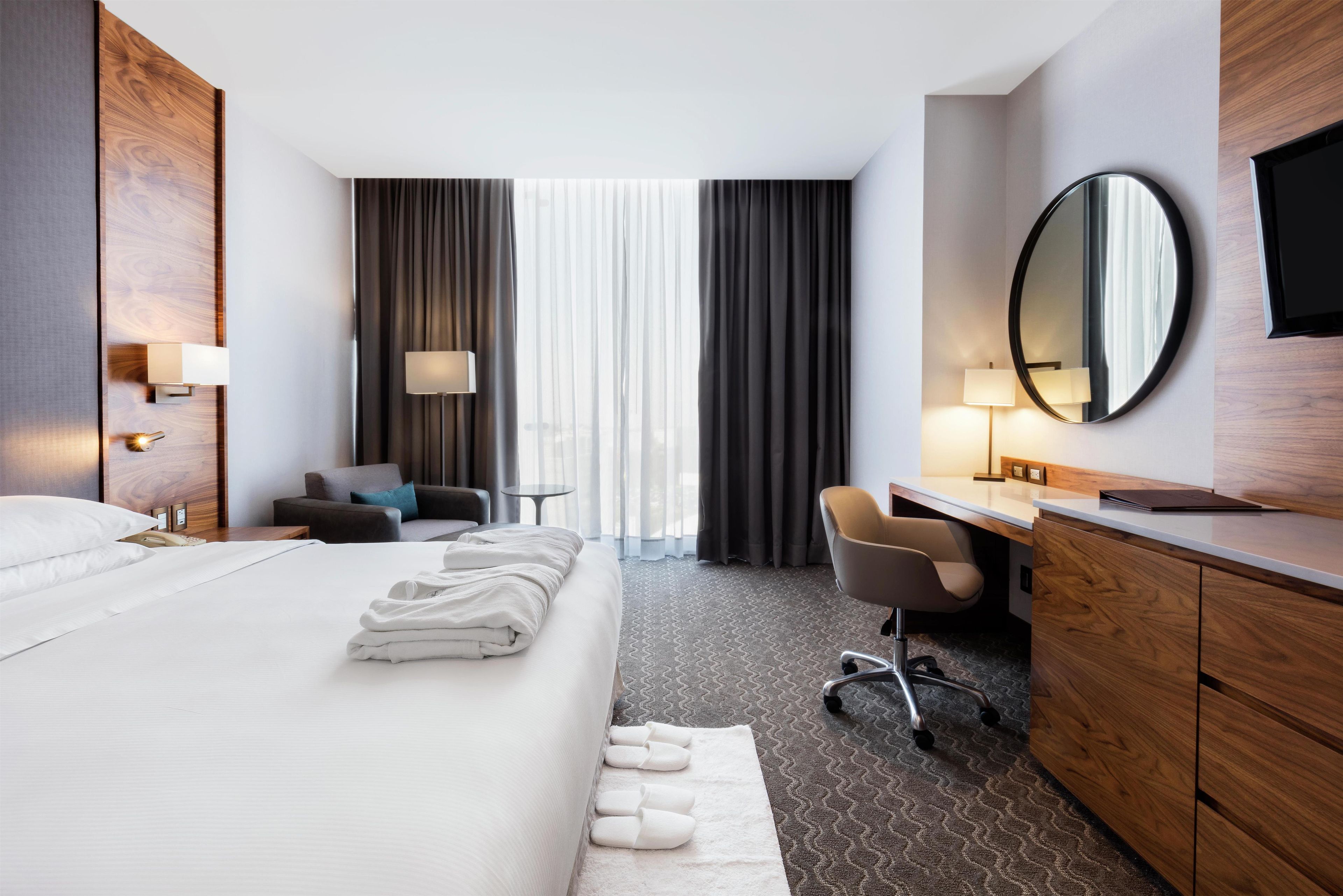 Une chambre d’hôtel avec un lit, un bureau, une chaise, une télévision et une grande fenêtre avec des rideaux.