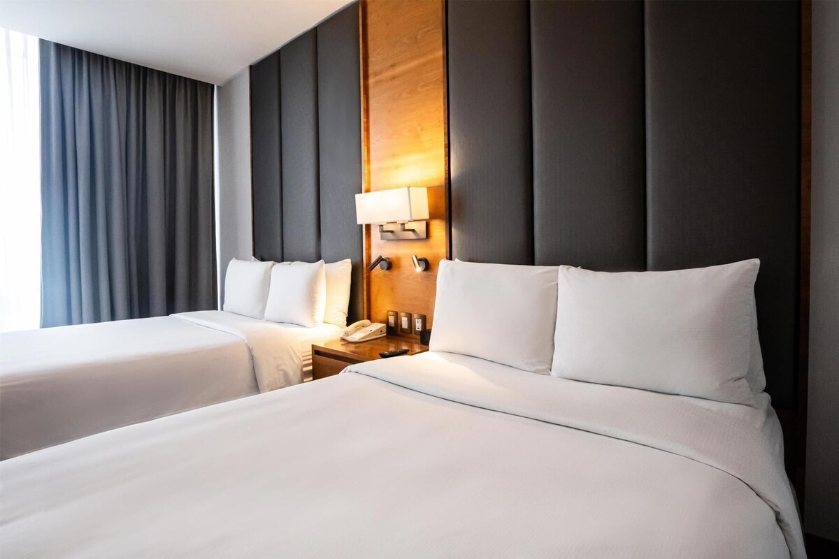 Une chambre d’hôtel avec deux lits, une tête de lit en bois, une table de chevet avec une lampe et un téléphone.