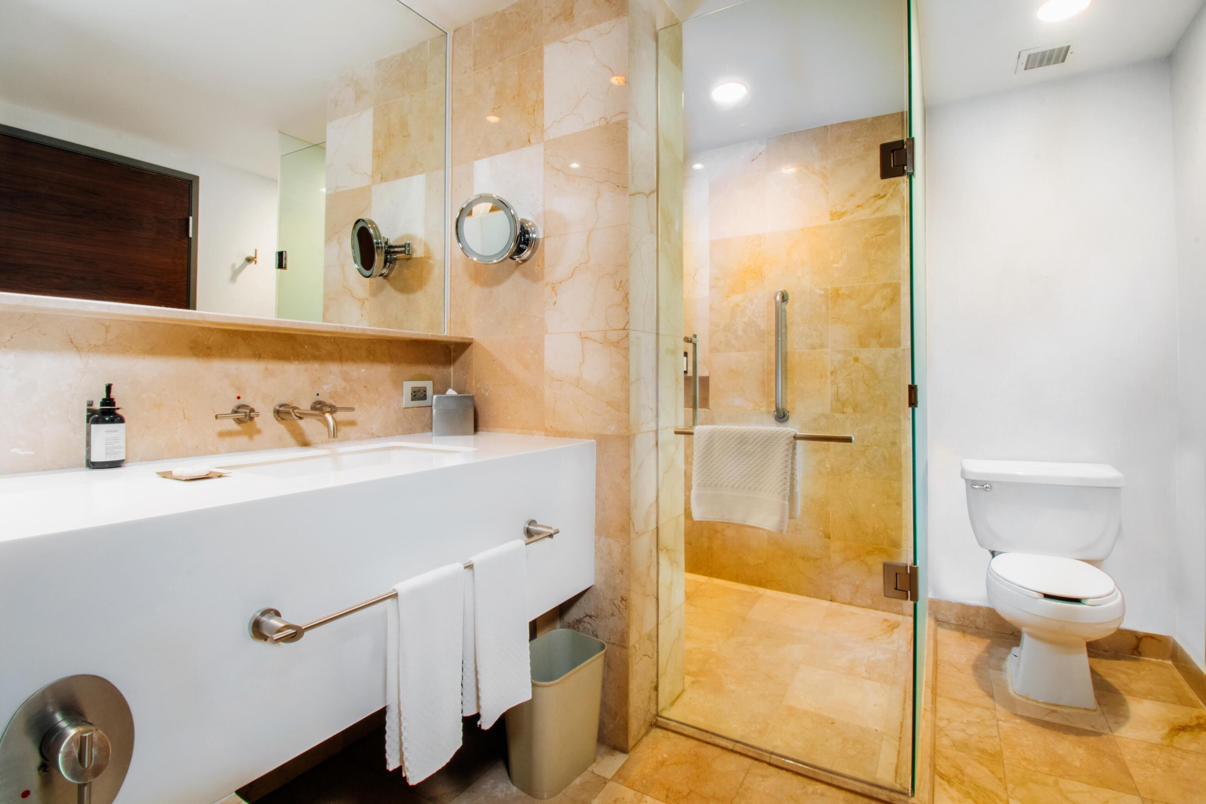 A modern bathroom with a glass-enclosed shower, a white sink with a marble countertop, and a toilet.